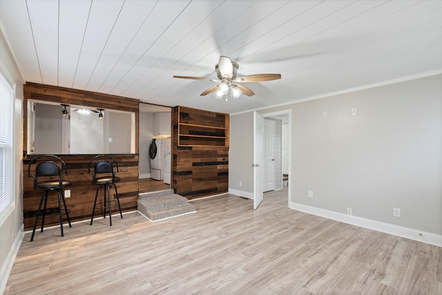 living area featuring crown molding, baseboards, washing machine and dryer, wood finished floors, and a ceiling fan