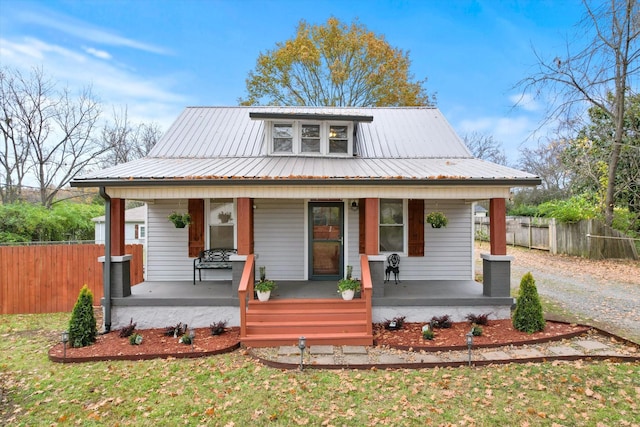 bungalow with metal roof, gravel driveway, covered porch, and fence