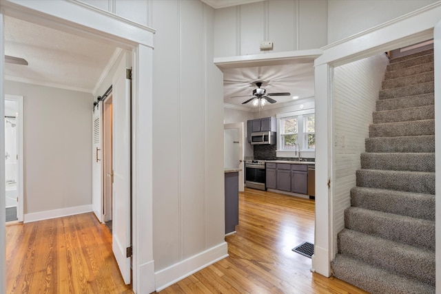 hall with a sink, stairway, light wood-style flooring, and crown molding