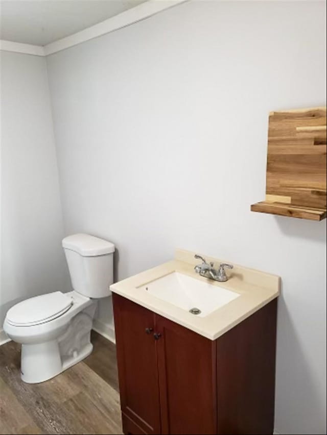 bathroom featuring toilet, ornamental molding, wood finished floors, baseboards, and vanity