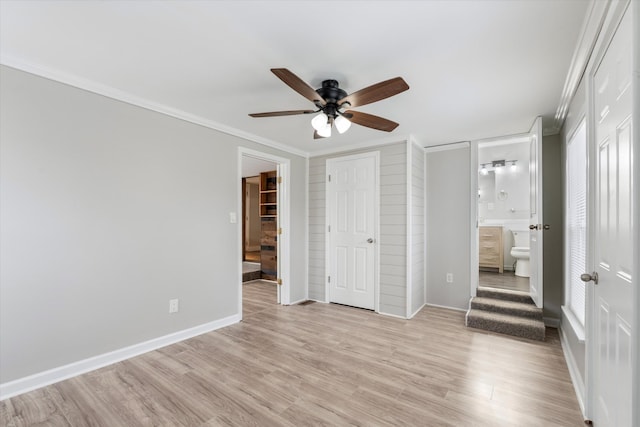 unfurnished bedroom with crown molding, baseboards, ensuite bathroom, light wood-style floors, and a ceiling fan