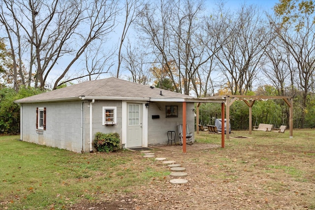 rear view of property featuring a pergola, a lawn, concrete block siding, and a shingled roof