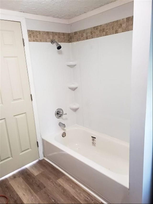 full bathroom with a textured ceiling, wood finished floors, and washtub / shower combination