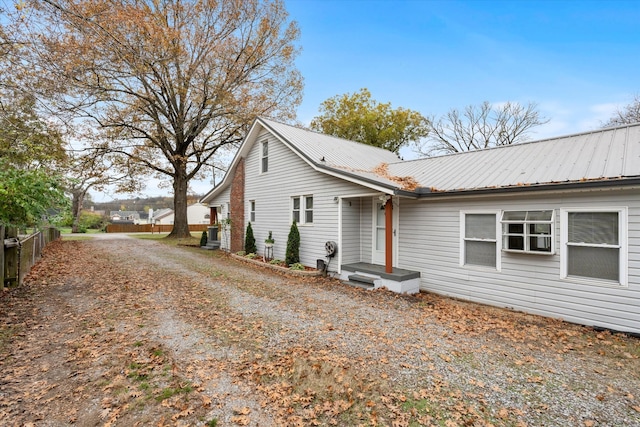 back of property featuring metal roof, dirt driveway, and fence