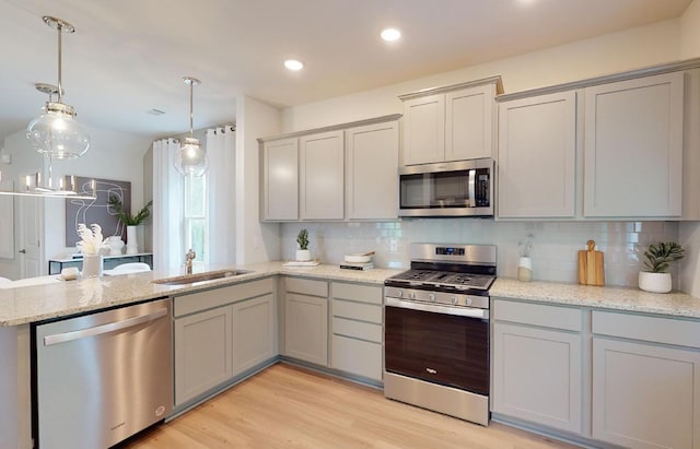 kitchen featuring backsplash, gray cabinetry, a peninsula, stainless steel appliances, and a sink