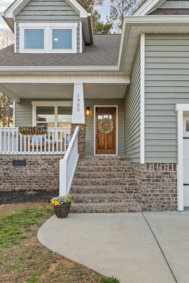 doorway to property featuring a porch and a shingled roof