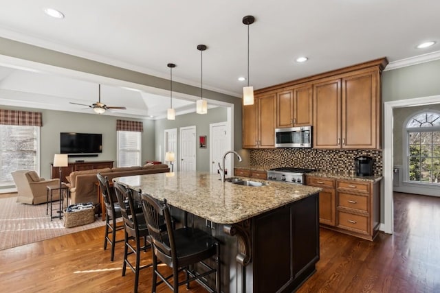 kitchen featuring stainless steel microwave, backsplash, brown cabinetry, stove, and a sink