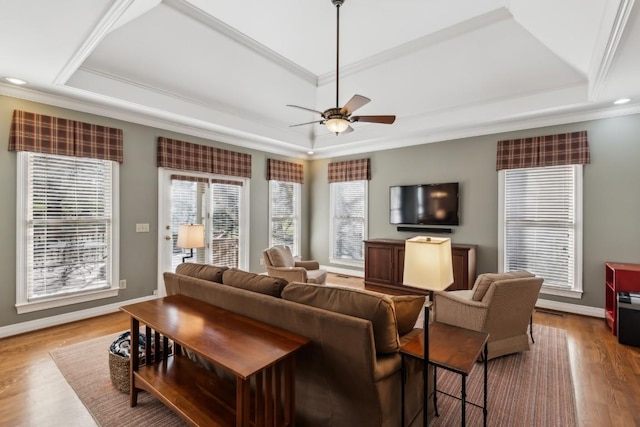 living area with wood finished floors, a ceiling fan, baseboards, ornamental molding, and a raised ceiling