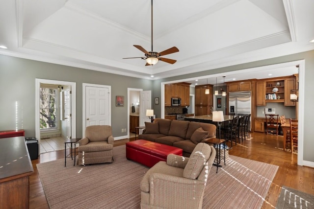 living room with baseboards, a ceiling fan, a tray ceiling, and wood finished floors