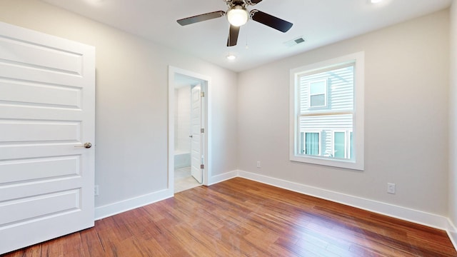 unfurnished bedroom with a ceiling fan, wood finished floors, visible vents, baseboards, and connected bathroom