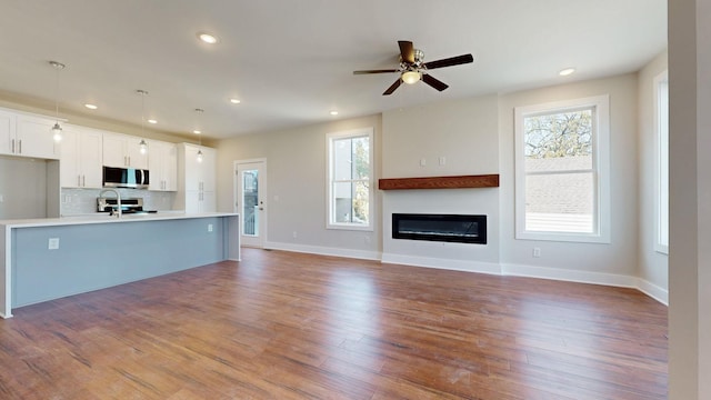 unfurnished living room with baseboards, recessed lighting, wood finished floors, a glass covered fireplace, and a ceiling fan