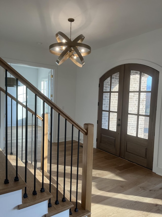 foyer featuring stairway, light wood-style floors, arched walkways, and french doors