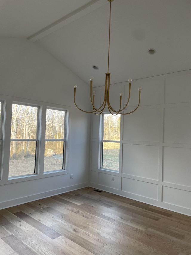 unfurnished dining area featuring light wood finished floors, visible vents, vaulted ceiling with beams, an inviting chandelier, and a decorative wall