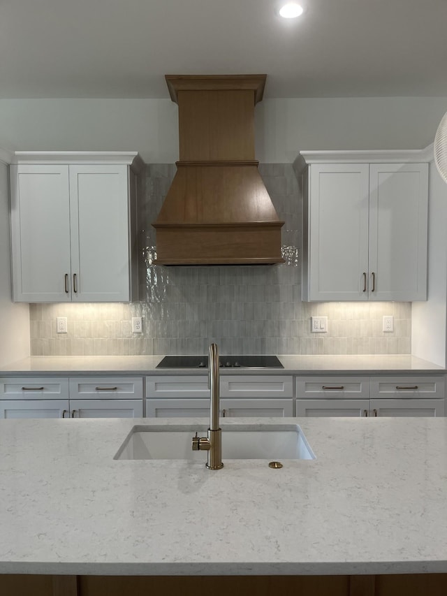 kitchen with premium range hood, black electric cooktop, decorative backsplash, and a sink