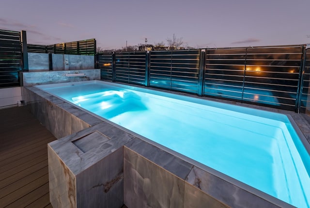 pool at dusk featuring a hot tub