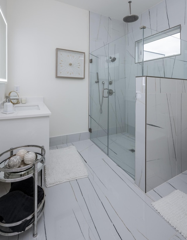 bathroom featuring a marble finish shower, baseboards, and a sink