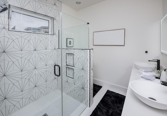 bathroom with a shower stall, double vanity, baseboards, and a sink