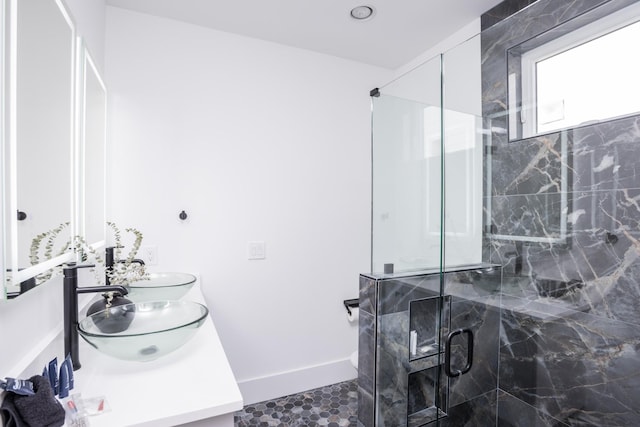 bathroom with double vanity, baseboards, a marble finish shower, and a sink