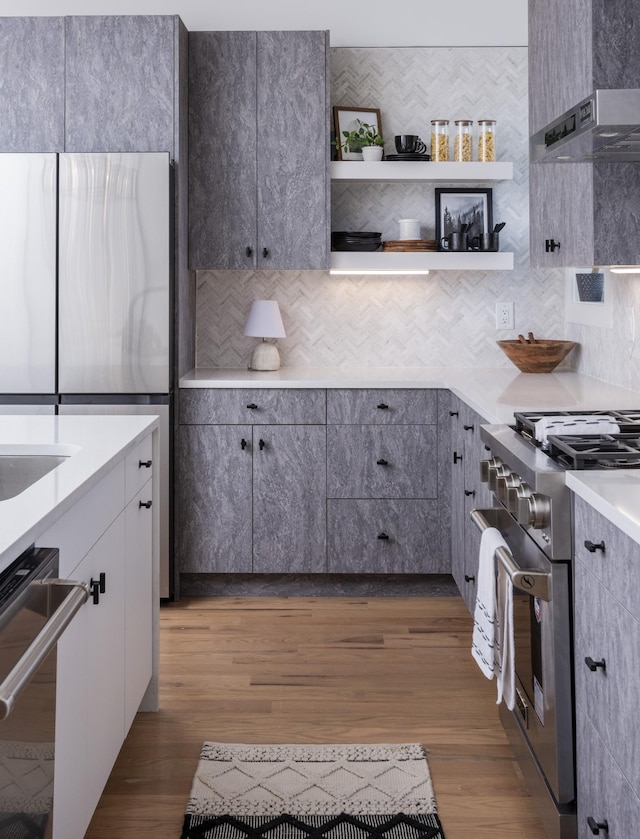 kitchen with dark wood-type flooring, open shelves, appliances with stainless steel finishes, light countertops, and decorative backsplash