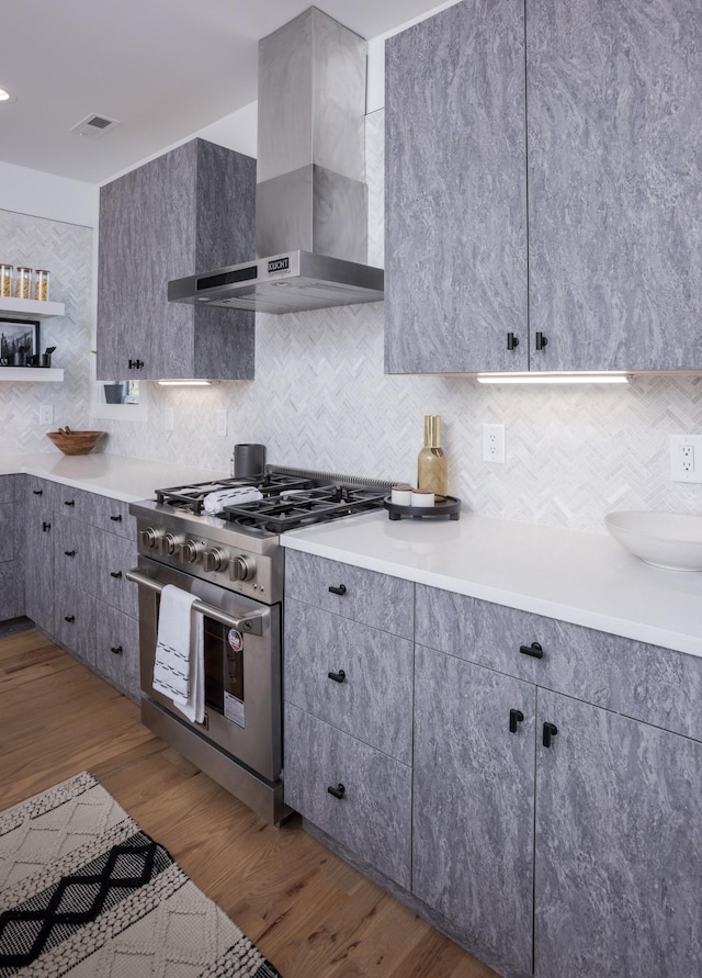 kitchen featuring gray cabinetry, high end stainless steel range, tasteful backsplash, wood finished floors, and wall chimney range hood