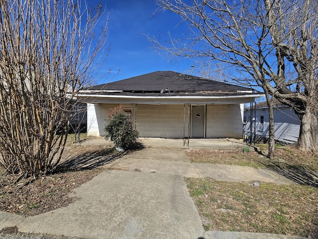 view of front of home with concrete block siding, covered porch, and roof with shingles