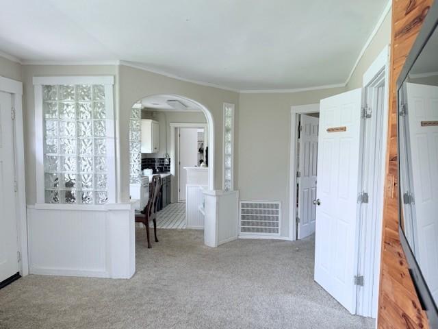 interior space with arched walkways, visible vents, light colored carpet, and crown molding