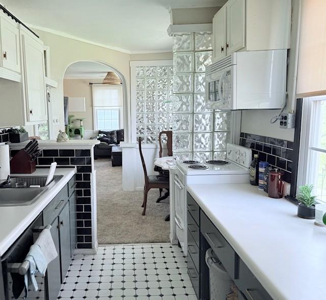 kitchen featuring range with electric stovetop, arched walkways, white cabinets, light countertops, and white microwave