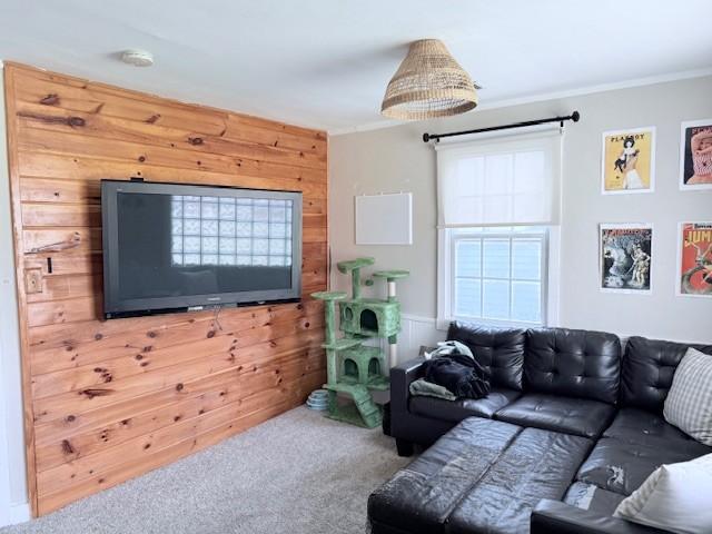 carpeted living room featuring wooden walls and ornamental molding