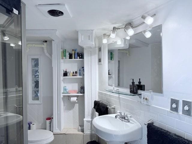 bathroom with a sink, toilet, and tile walls