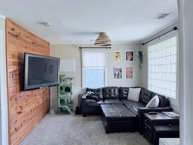 carpeted living area with a wealth of natural light, visible vents, and wood walls