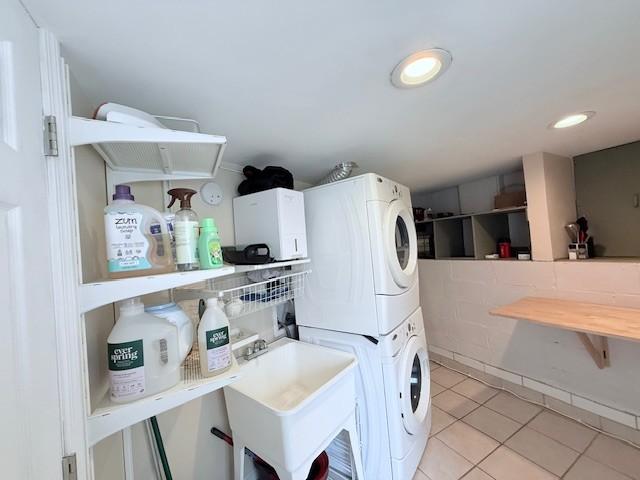 laundry room featuring stacked washer and dryer, a sink, recessed lighting, light tile patterned flooring, and laundry area