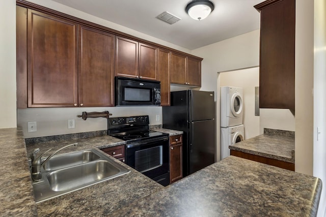 kitchen featuring visible vents, a sink, black appliances, stacked washer and dryer, and dark countertops