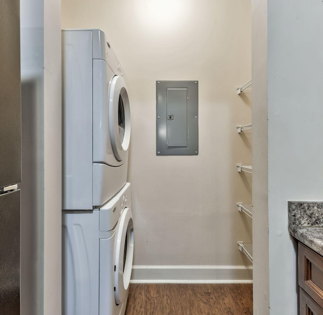 laundry room featuring baseboards, electric panel, laundry area, stacked washer and clothes dryer, and wood finished floors