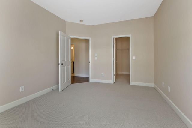 unfurnished bedroom with a walk in closet, carpet flooring, baseboards, and a closet