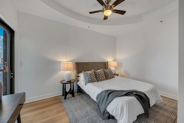 bedroom featuring a tray ceiling, light wood-type flooring, baseboards, and a ceiling fan