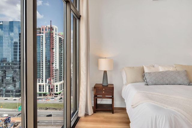 bedroom with light wood finished floors, a city view, and baseboards