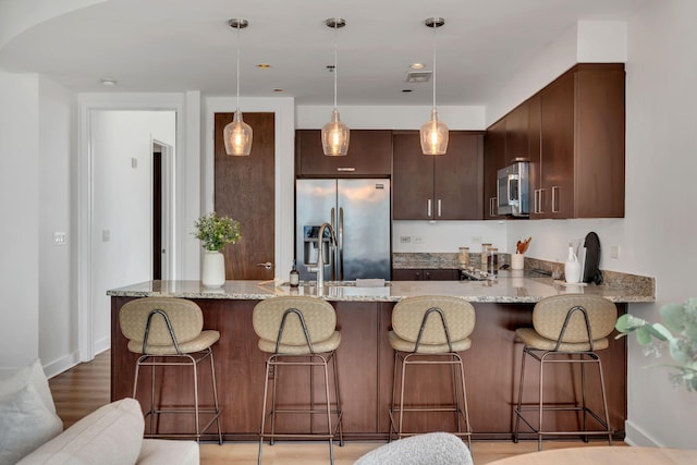 kitchen with dark brown cabinetry, pendant lighting, light stone counters, appliances with stainless steel finishes, and a peninsula