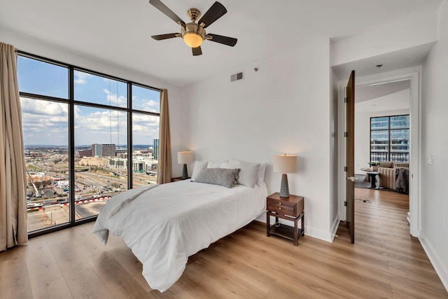 bedroom featuring visible vents, baseboards, light wood-style flooring, access to exterior, and a view of city