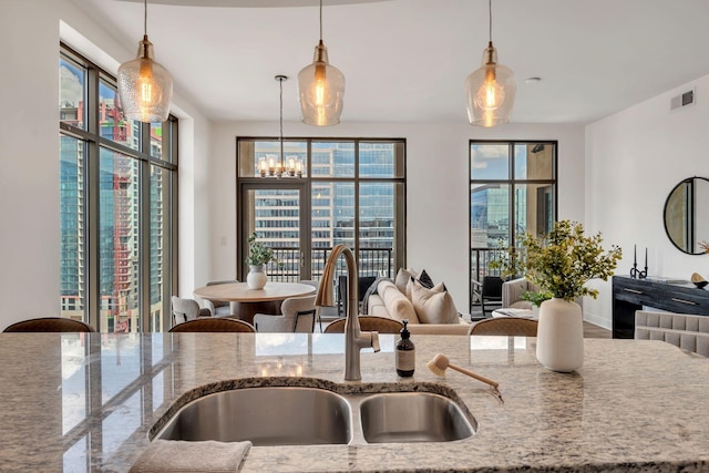 kitchen featuring visible vents, decorative light fixtures, light stone counters, an inviting chandelier, and a sink