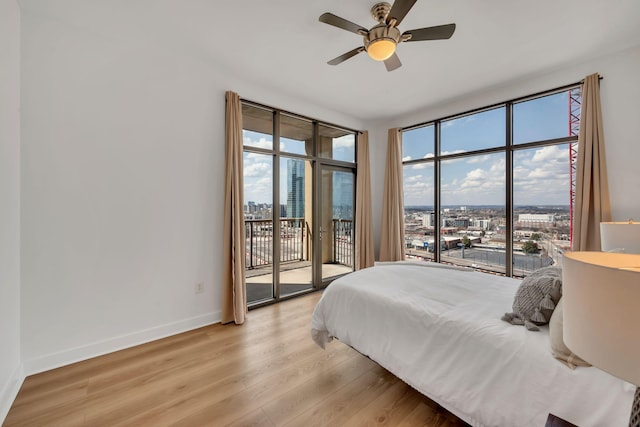 bedroom with access to exterior, light wood finished floors, ceiling fan, baseboards, and a view of city