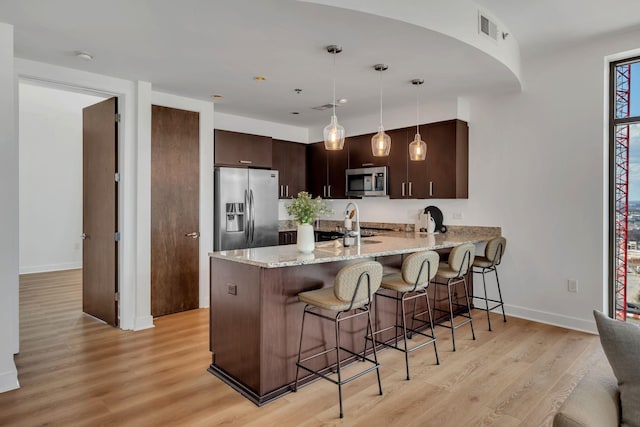 kitchen featuring visible vents, dark brown cabinetry, appliances with stainless steel finishes, a breakfast bar area, and a peninsula