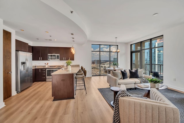 kitchen featuring a peninsula, stainless steel appliances, dark brown cabinetry, a kitchen bar, and open floor plan