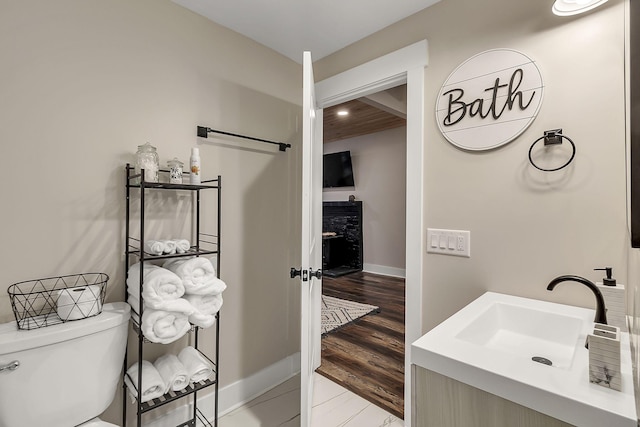 half bath with wood finished floors, toilet, baseboards, and a sink