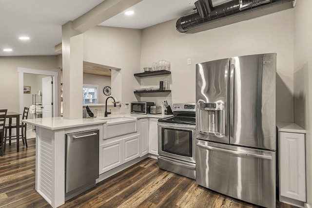 kitchen with open shelves, a peninsula, a sink, light countertops, and appliances with stainless steel finishes