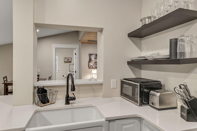 kitchen with open shelves, white cabinetry, light countertops, and a sink