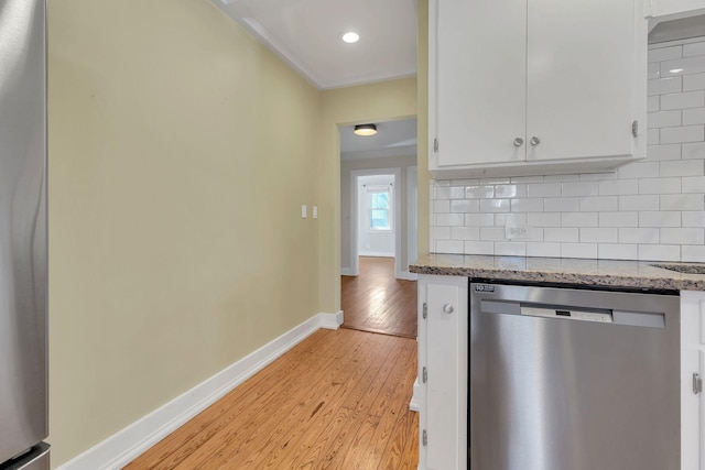 kitchen with white cabinets, light wood finished floors, decorative backsplash, baseboards, and dishwasher