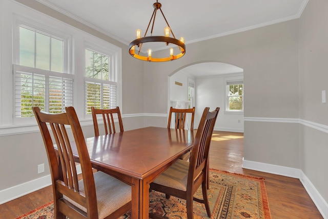 dining area with wood finished floors, arched walkways, a chandelier, and ornamental molding