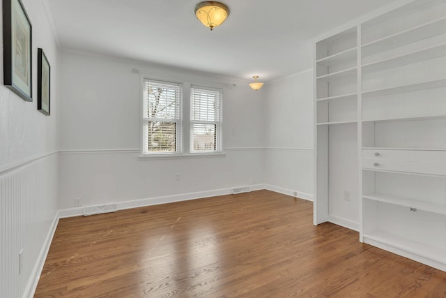 empty room featuring a wainscoted wall, wood finished floors, and visible vents