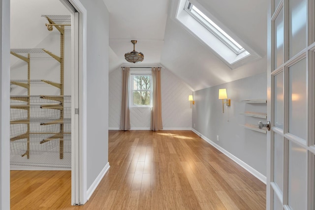 foyer entrance featuring vaulted ceiling with skylight, baseboards, and light wood-type flooring