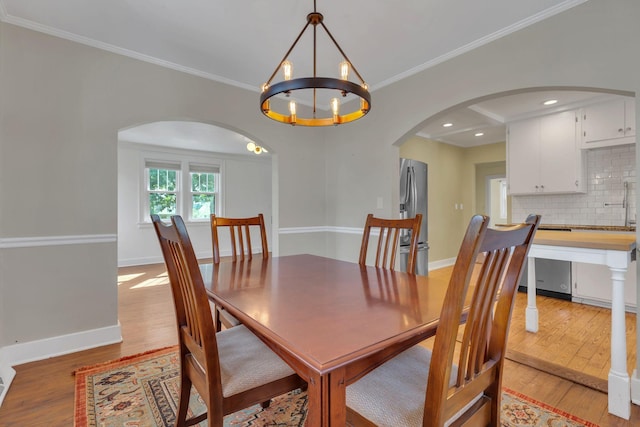 dining room with light wood-type flooring, arched walkways, crown molding, baseboards, and a chandelier